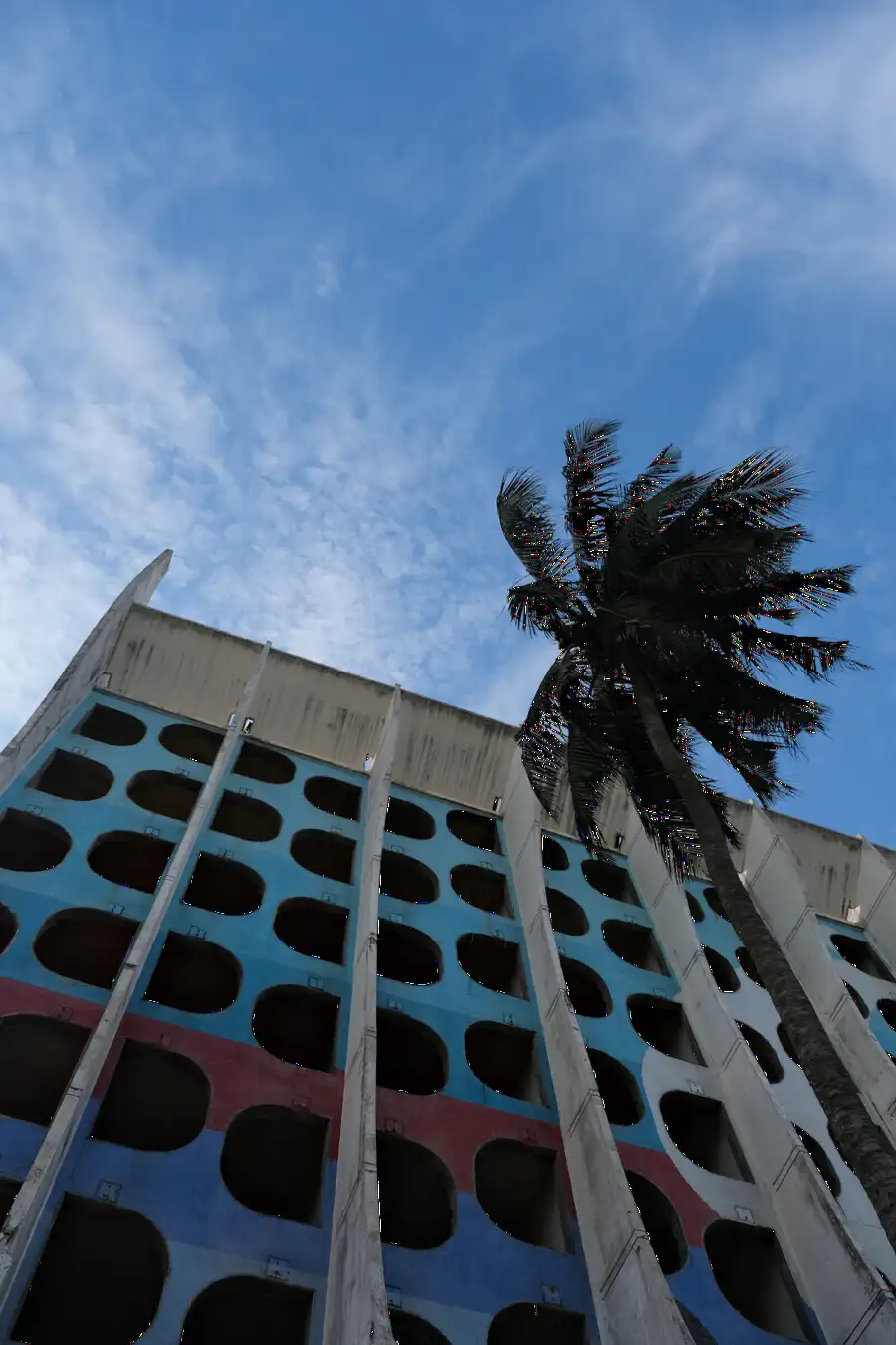 Façade d’un immeuble de Lomé vue en contre-plongée avec un palmier sous un ciel bleu